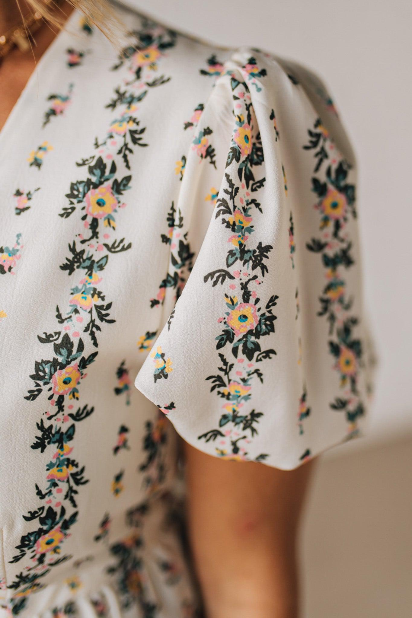 Blonde woman wearing a floral print tie front shirred hem blouse top with puff sleeve.