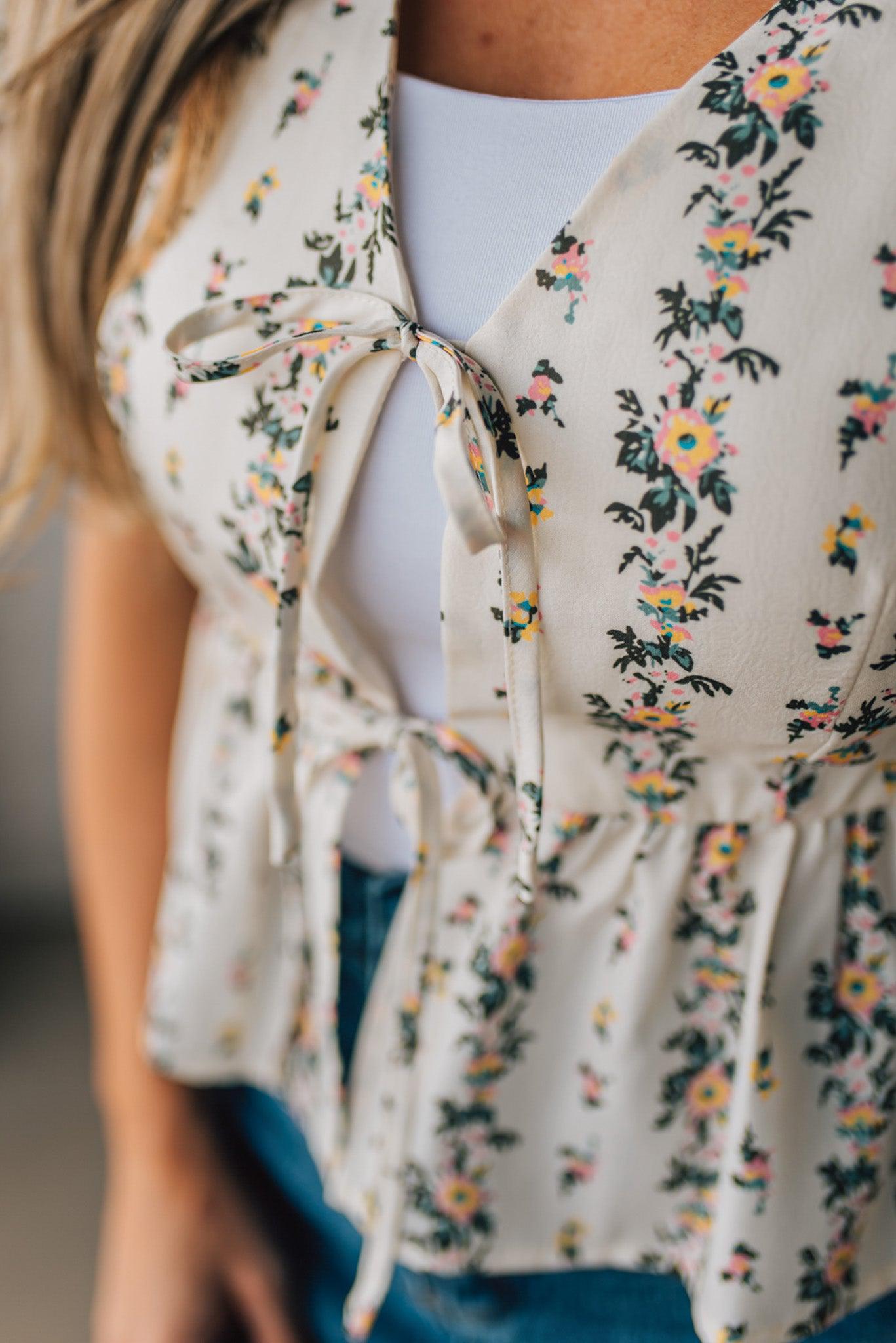 Blonde woman wearing a floral print tie front shirred hem blouse top with puff sleeve.