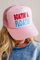 Pink trucker hat with 'Boatin' & Floatin' text worn by a person with blonde hair.