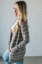 Woman wearing a gray striped cardigan against a white brick wall.