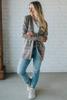 Woman wearing a plaid cardigan, white shirt, blue jeans, and white sneakers against a white brick wall.
