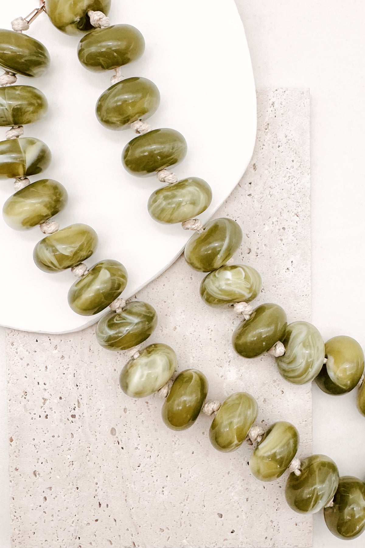 A CHUNKY BEADED NECKLACE WITH KNOTS BETWEEN EACH BEAD IN A GREEN MARBLED TONE.