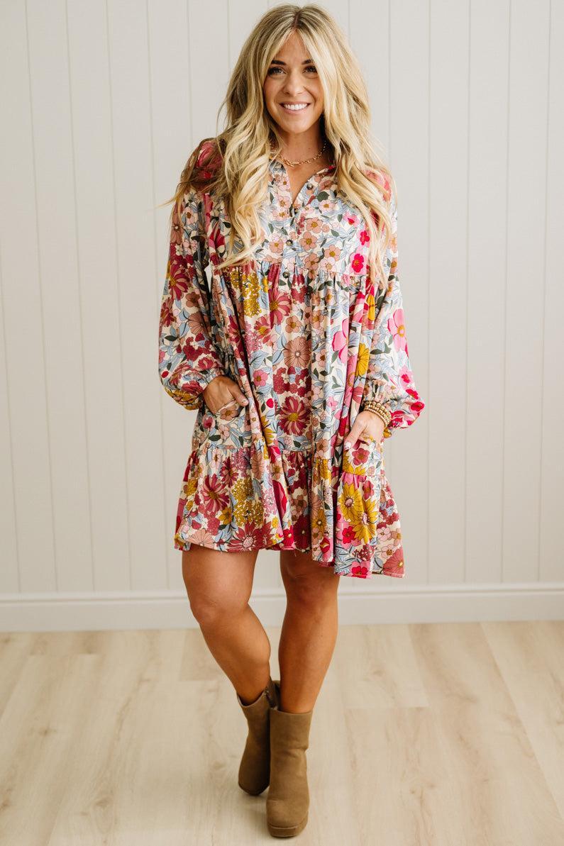 Woman wearing a floral dress with long sleeves against a white paneled wall.