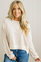 Woman wearing a cream sweater and blue jeans against a white wall