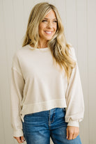Woman wearing a beige sweater and blue jeans against a light wooden panel background