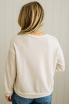 Person wearing a beige sweatshirt and blue jeans against a white paneled wall.