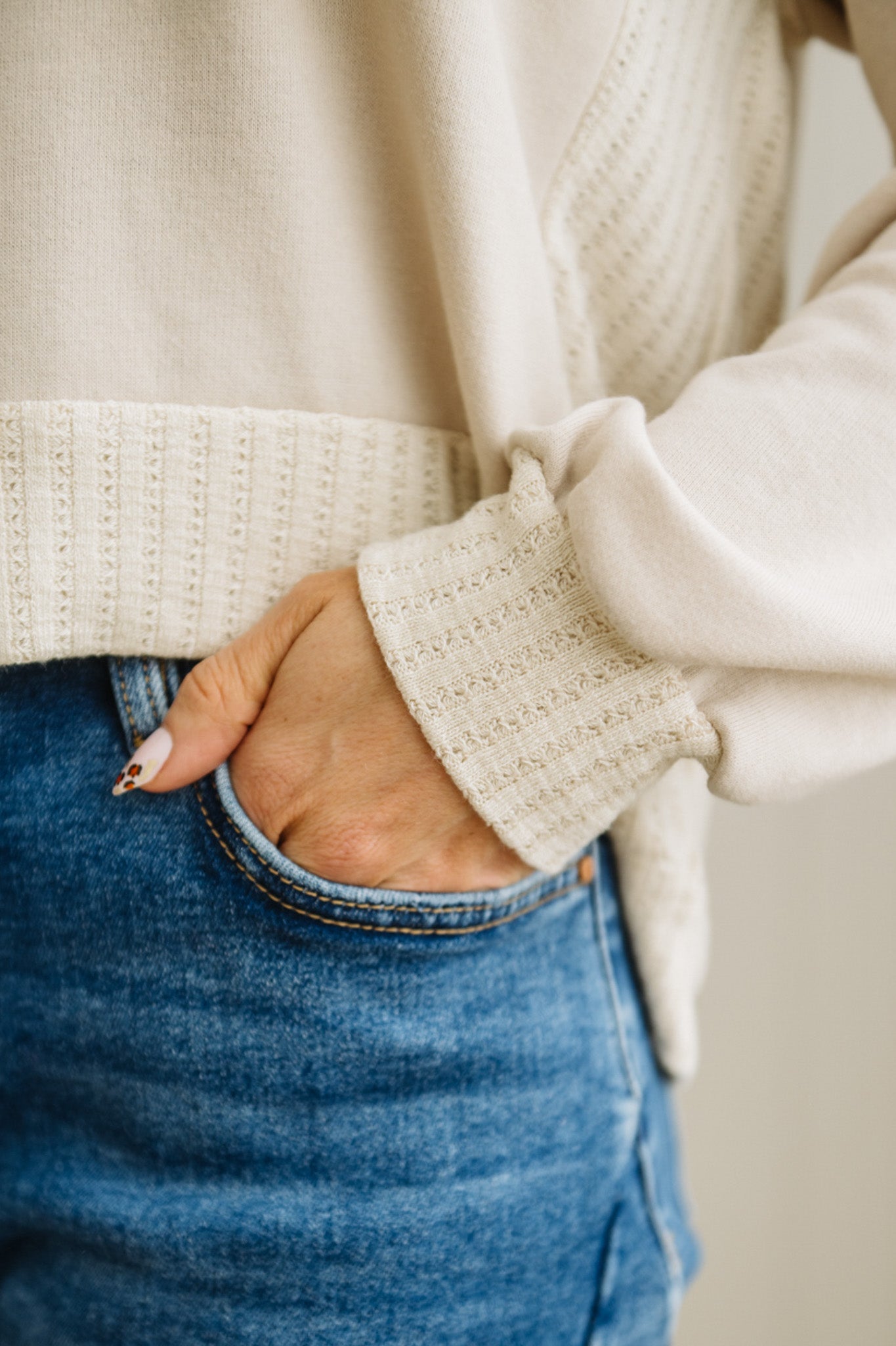 Close-up of a person wearing a white sweater and blue jeans with a neutral background