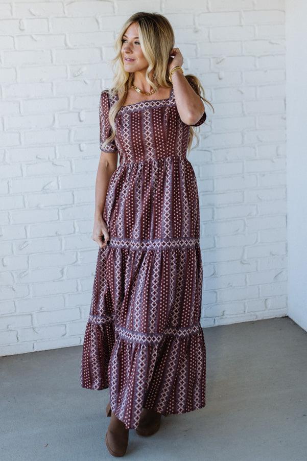 Woman wearing a patterned dress against a white brick wall.