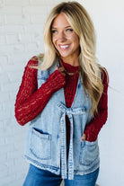 Woman wearing a denim vest over a red sweater with a white brick wall background