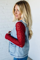 Woman wearing red knitted arm warmers against a white brick wall.