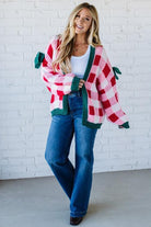 Woman wearing a plaid cardigan with green accents against a white brick wall.