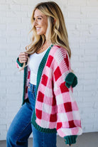 Woman wearing a colorful plaid cardigan with a white brick wall background