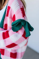 Person wearing a colorful sweater with heart patterns and green gloves.