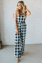 Woman wearing a black and white checkered jumpsuit against a white brick wall.