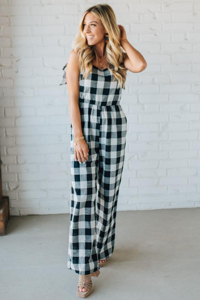 Woman wearing a black and white checkered jumpsuit against a white brick wall.