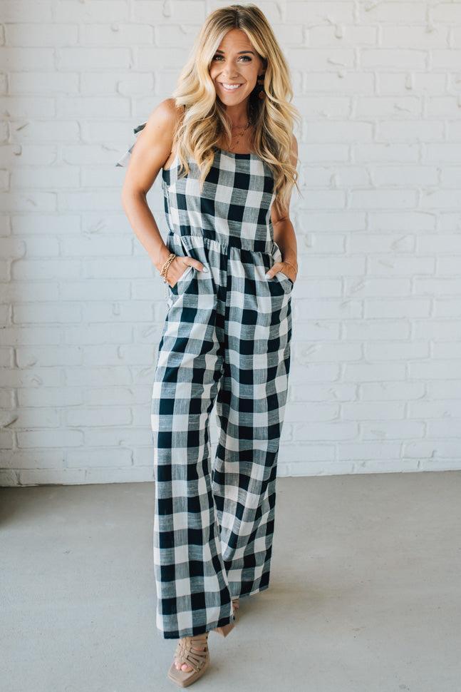 Woman wearing a black and white checkered jumpsuit against a white brick wall.