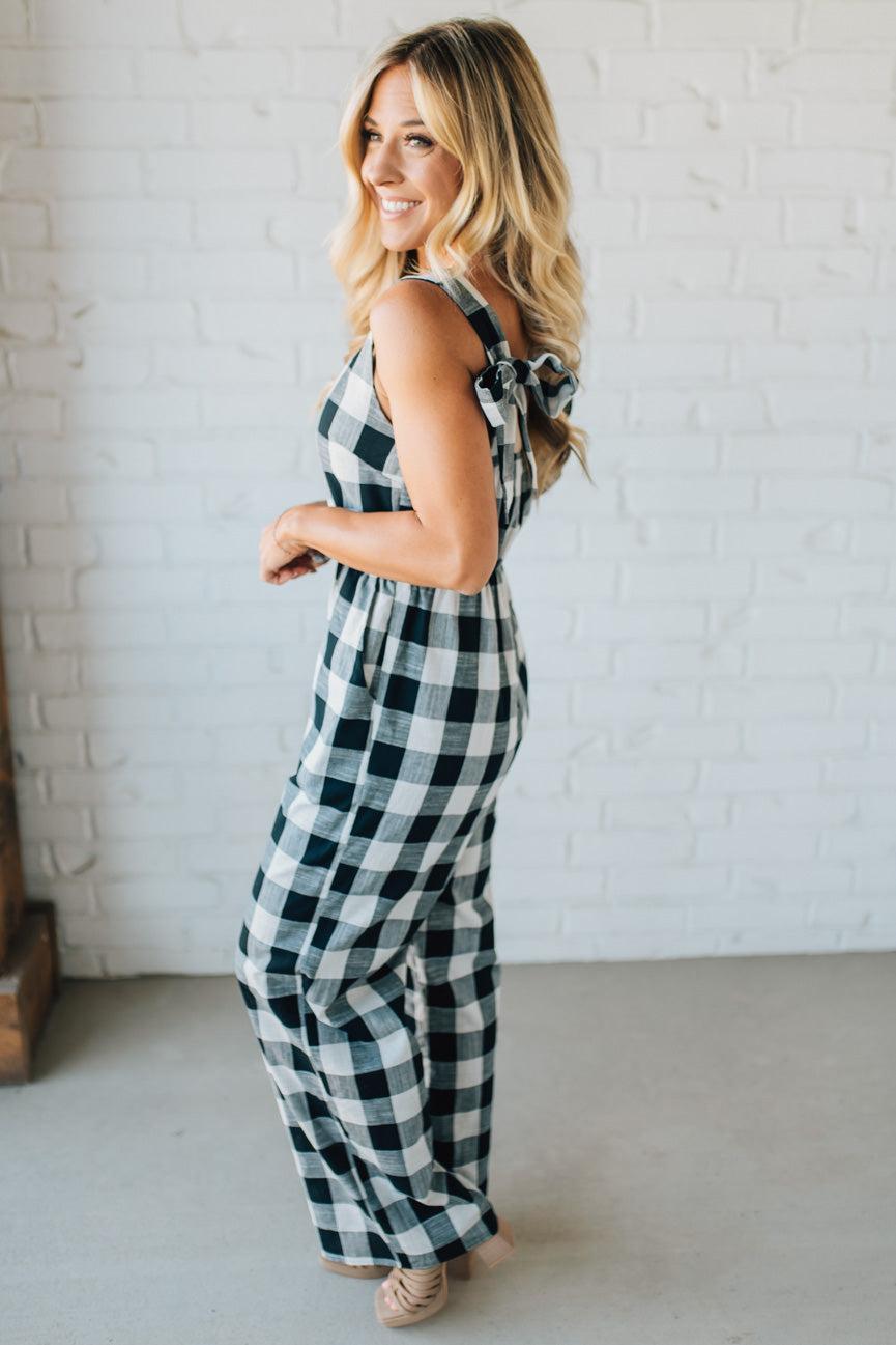 Woman wearing a black and white checkered jumpsuit standing against a white brick wall.