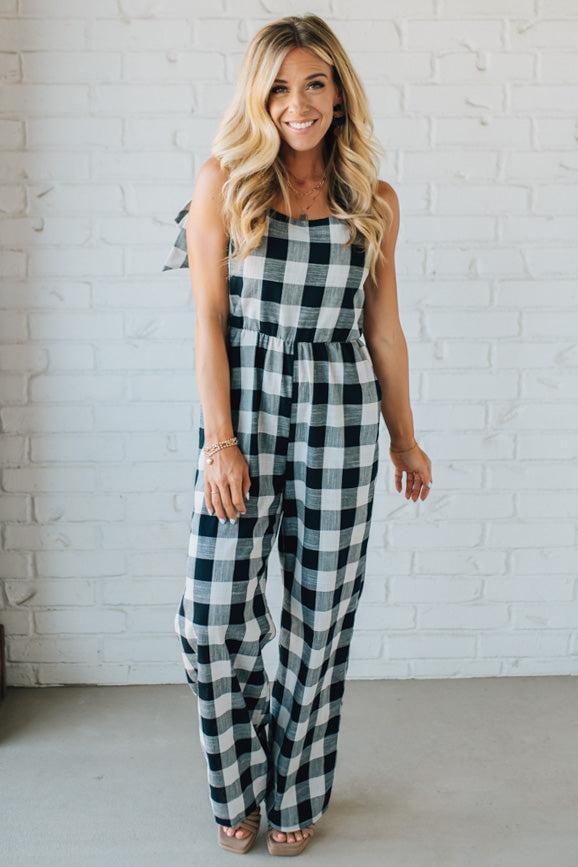 Woman wearing a black and white checkered jumpsuit against a white brick wall.