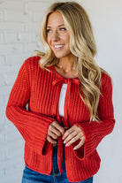 Woman wearing a red knitted cardigan against a white brick wall