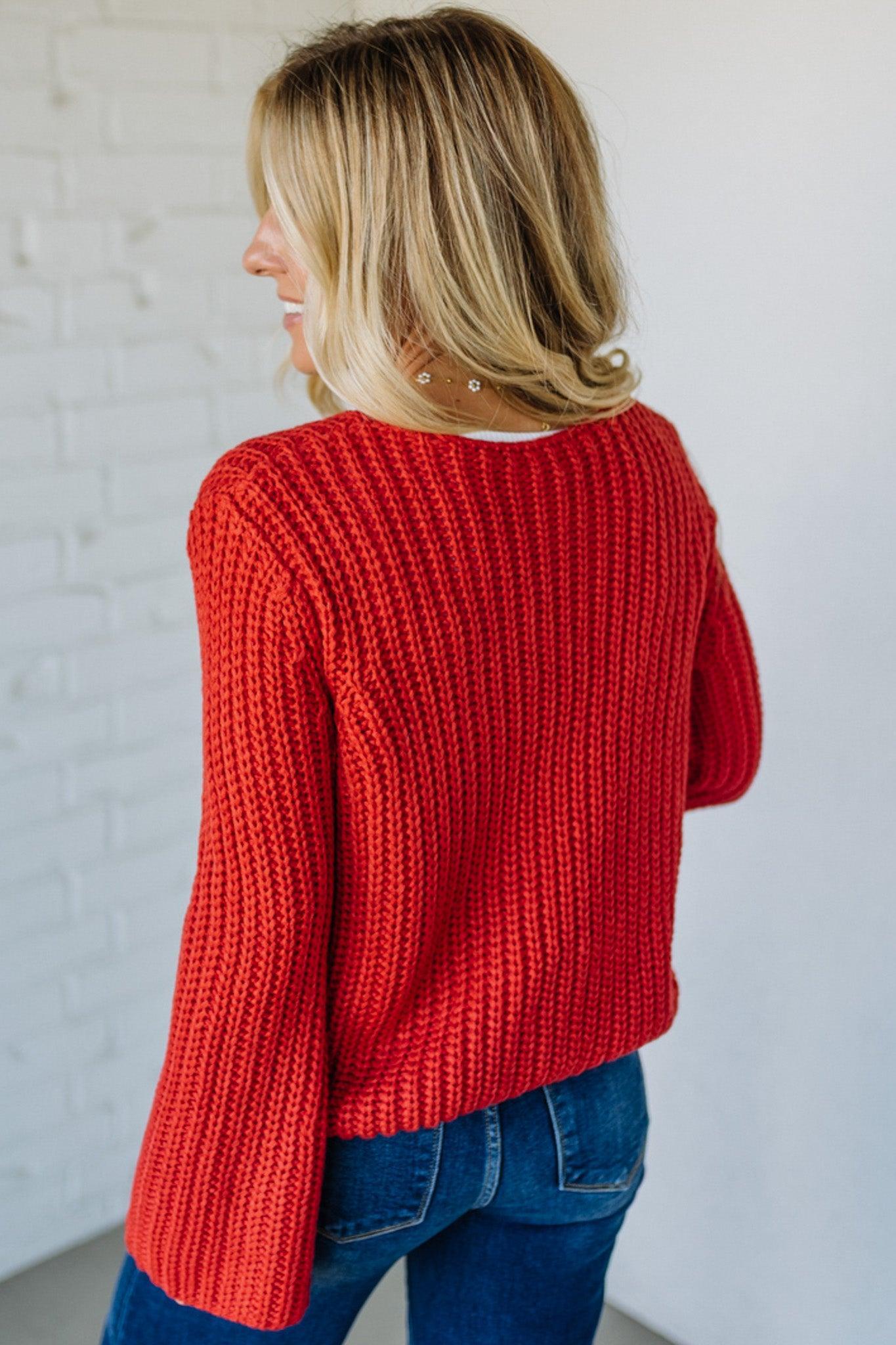 Person wearing a red knitted sweater and blue jeans against a white background