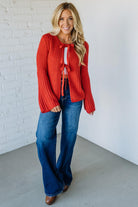 Woman wearing a red sweater and blue jeans against a white brick wall.