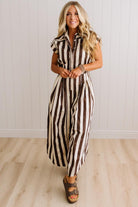 BLONDE WOMAN WEARING A SLEEVELESS WIDE LEG, WIDE STRIPE JUMPSUIT STANDING ON A LIGHT WOOD FLOOR AND NEUTRAL WALL BEHIND.