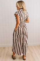 BLONDE WOMAN WEARING A SLEEVELESS WIDE LEG, WIDE STRIPE JUMPSUIT STANDING ON A LIGHT WOOD FLOOR AND NEUTRAL WALL BEHIND.
