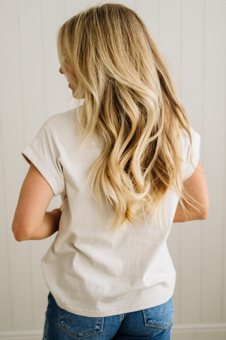 Person wearing a white t-shirt and blue jeans with long blonde hair, standing against a neutral background.