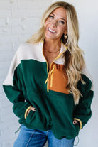 Woman wearing a green, white, and brown color-blocked jacket against a white brick wall.