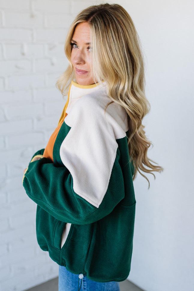 Woman wearing a green and white sweater against a white brick wall.