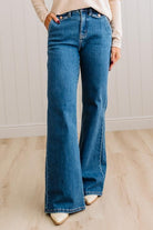 WOMAN WEARING HIGH RISE FLARE JEANS IN A DARK WASH AND BUTTON FLAP SMALL POCKETS AT THE HIP.