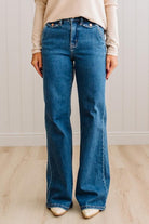 WOMAN WEARING HIGH RISE FLARE JEANS IN A DARK WASH AND BUTTON FLAP SMALL POCKETS AT THE HIP.