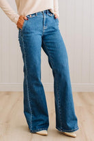 WOMAN WEARING HIGH RISE FLARE JEANS IN A DARK WASH AND BUTTON FLAP SMALL POCKETS AT THE HIP.