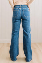 WOMAN WEARING HIGH RISE FLARE JEANS IN A DARK WASH AND BUTTON FLAP SMALL POCKETS AT THE HIP.