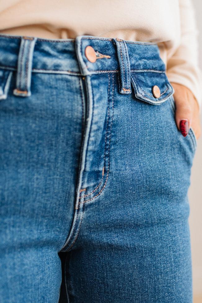 WOMAN WEARING HIGH RISE FLARE JEANS IN A DARK WASH AND BUTTON FLAP SMALL POCKETS AT THE HIP.