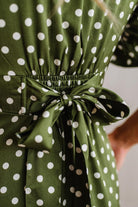 Close-up of an olive green dress with white polka dots, featuring a smocked waist and a matching fabric tie bow.
