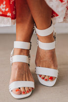 White wood block heels with faux leather wrap around straps and silver hardware accents.