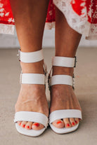 White wood block heels with faux leather wrap around straps and silver hardware accents.