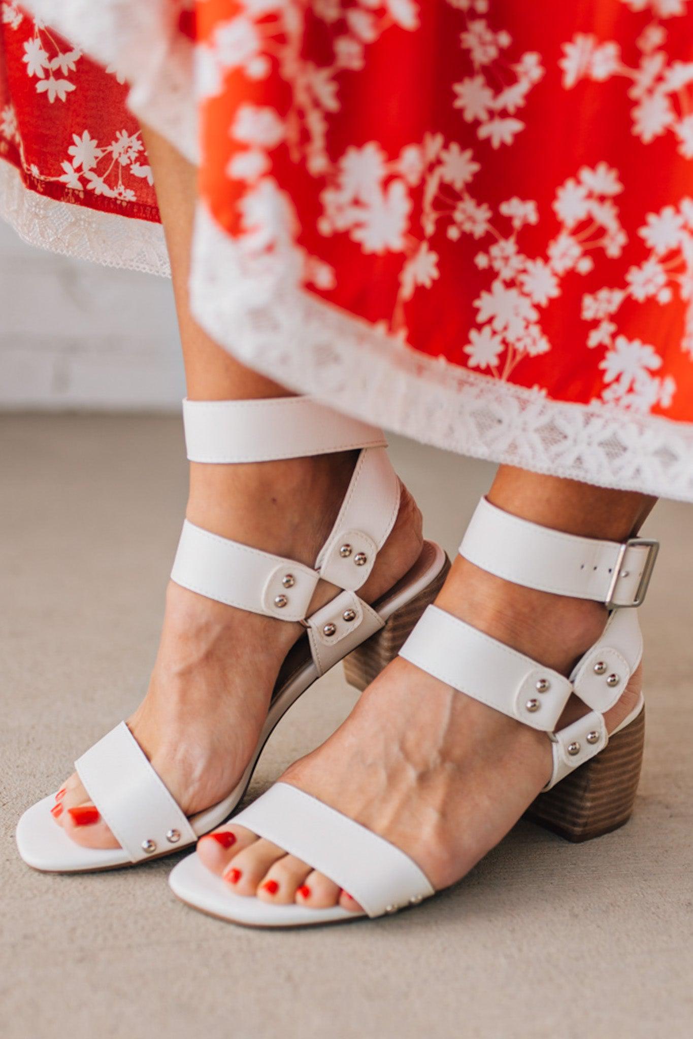 White wood block heels with faux leather wrap around straps and silver hardware accents.