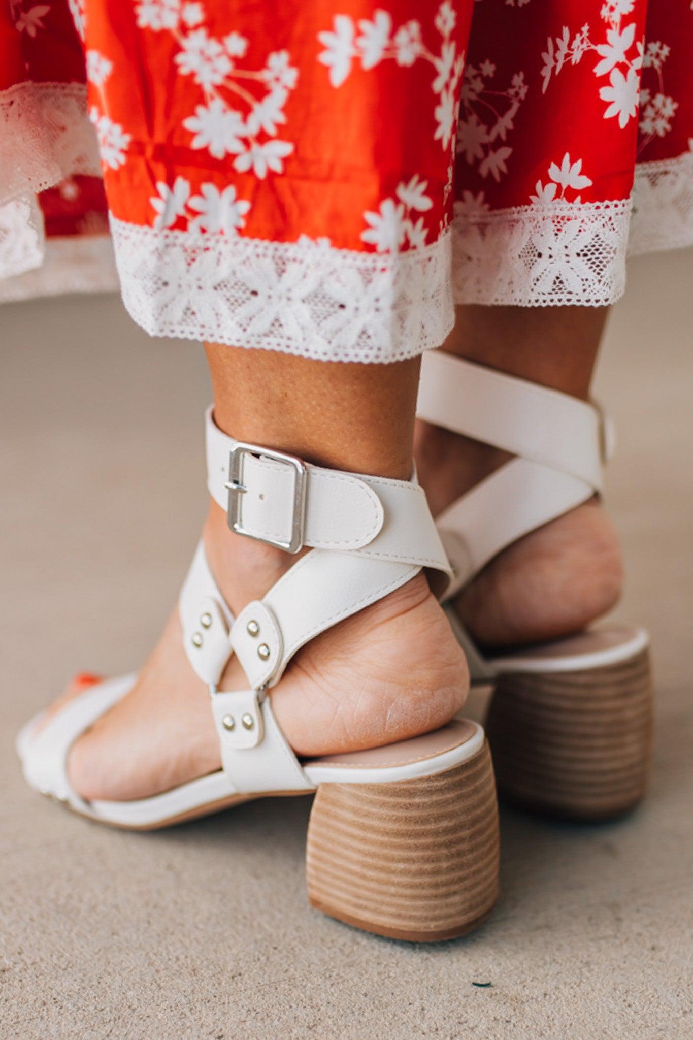 White wood block heels with faux leather wrap around straps and silver hardware accents.