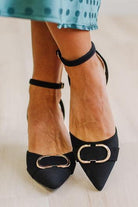 WOMAN IN A GREEN POLKA DOT DRESS WITH BLACK LOW HEELS, POINTED TOE , ANKLE STRAP AND GOLD BUCKLE ACCENT.