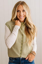BLONDE WOMAN WEARING A MOCK NECK,  FRONT BUTTON DETAILED, WITH CAP SLEEVES AND STRIPES. STANDING IN A WELL LIT STUDIO.

