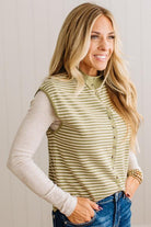 BLONDE WOMAN WEARING A MOCK NECK,  FRONT BUTTON DETAILED, WITH CAP SLEEVES AND STRIPES. STANDING IN A WELL LIT STUDIO.