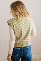 BLONDE WOMAN WEARING A MOCK NECK,  FRONT BUTTON DETAILED, WITH CAP SLEEVES AND STRIPES. STANDING IN A WELL LIT STUDIO.