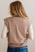 BLONDE WOMAN WEARING A MOCK NECK,  FRONT BUTTON DETAILED, WITH CAP SLEEVES AND STRIPES. STANDING IN A WELL LIT STUDIO.