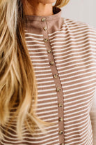 BLONDE WOMAN WEARING A MOCK NECK,  FRONT BUTTON DETAILED, WITH CAP SLEEVES AND STRIPES. STANDING IN A WELL LIT STUDIO.