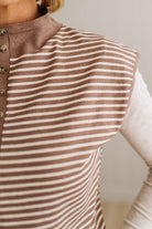 BLONDE WOMAN WEARING A MOCK NECK,  FRONT BUTTON DETAILED, WITH CAP SLEEVES AND STRIPES. STANDING IN A WELL LIT STUDIO.