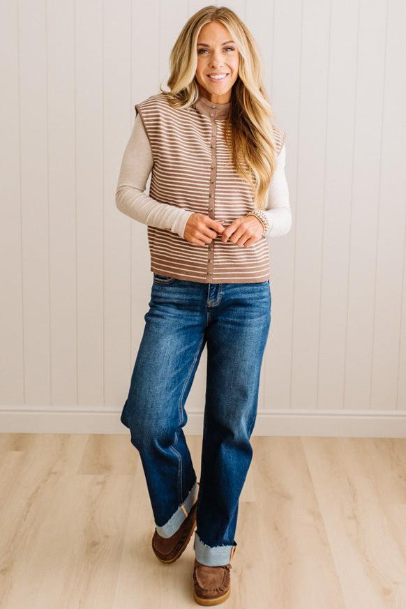 BLONDE WOMAN WEARING A MOCK NECK,  FRONT BUTTON DETAILED, WITH CAP SLEEVES AND STRIPES. STANDING IN A WELL LIT STUDIO.