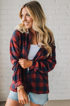 Woman wearing a red and black plaid shirt with denim shorts against a white brick wall.