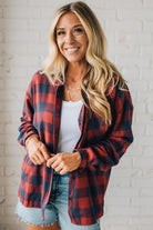 Woman wearing a red and black plaid shirt against a white brick wall